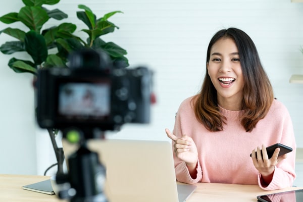 A content creator smiles while they film themselves sitting at a desk, explaining a process.
