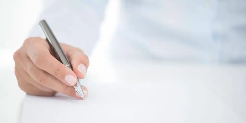 A person uses a silver pen to write on a piece of paper.